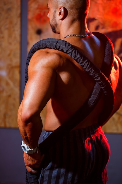 Hombre fuerte guapo deportivo posando con cuerda de deportes en el fondo del gimnasio. Un culturista fuerte con abdominales, hombros, bíceps, tríceps y pecho perfectos.