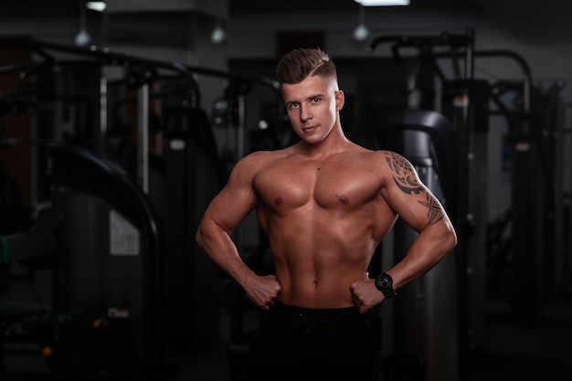 Hombre fuerte y guapo modelo de fitness con cuerpo deportivo y tatuaje en la mano hace ejercicio en el gimnasio