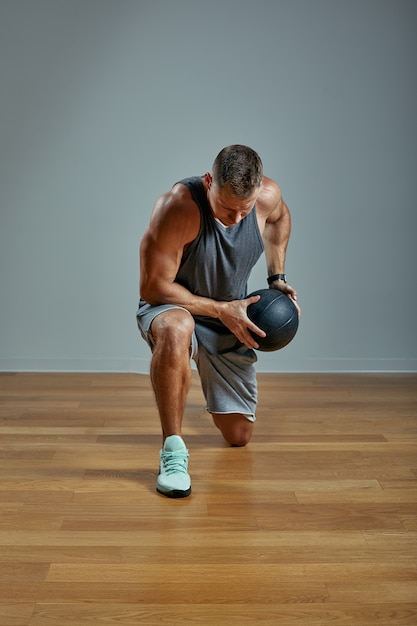 Hombre fuerte haciendo ejercicio con balón med. Foto del físico perfecto del hombre en la pared gris. Fuerza y motivación.