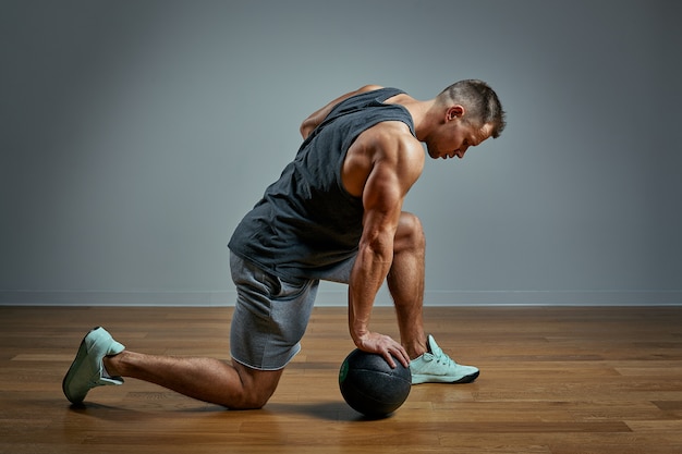 Hombre fuerte haciendo ejercicio con balón med. Foto del físico perfecto del hombre sobre fondo gris. Fuerza y motivación.