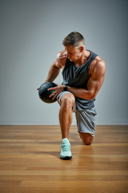 Hombre fuerte haciendo ejercicio con balón med. hombre físico perfecto en gris. Fuerza y motivación.