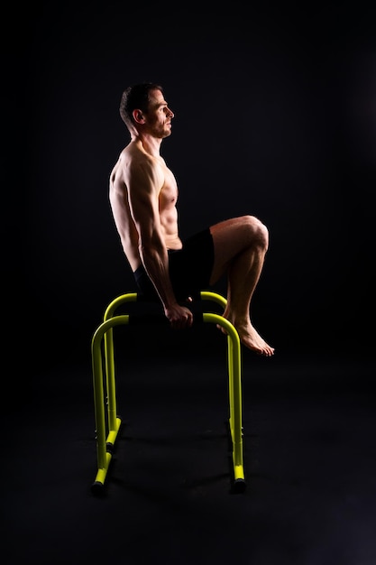 Hombre fuerte haciendo ejercicios deportivos en barras horizontales y paralelas, dominadas en barras paralelas