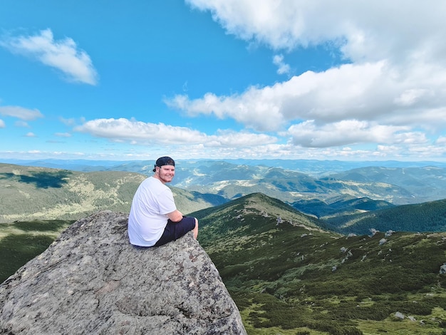 Hombre fuerte joven sentado en la roca en la cima del pico de la montaña disfrutando de la vista. concepto de senderismo