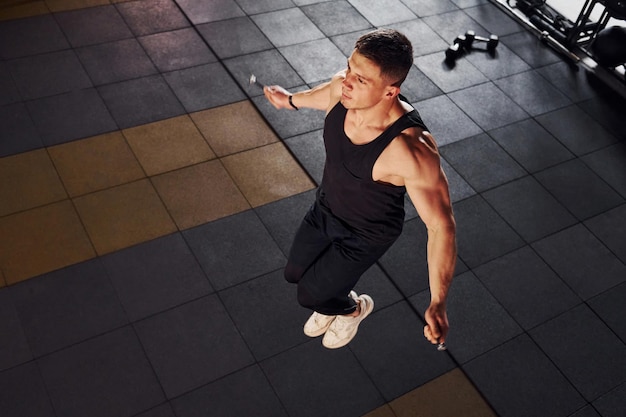 Un hombre fuerte con ropa deportiva tiene un día de entrenamiento en el gimnasio usando una cuerda para saltar