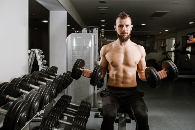 Hombre fuerte sentado y levantando pesas en el gimnasio