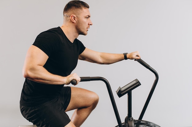 Hombre fuerte usando bicicleta de aire para entrenamiento cardiovascular en el gimnasio de entrenamiento cruzado