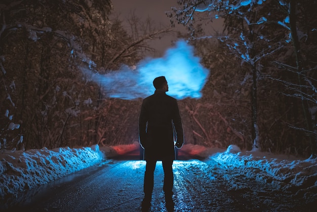 El hombre fuma en el camino nevado en el bosque. tarde noche