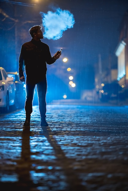 El hombre fuma cigarrillo eléctrico en la calle. Por la noche, por la noche