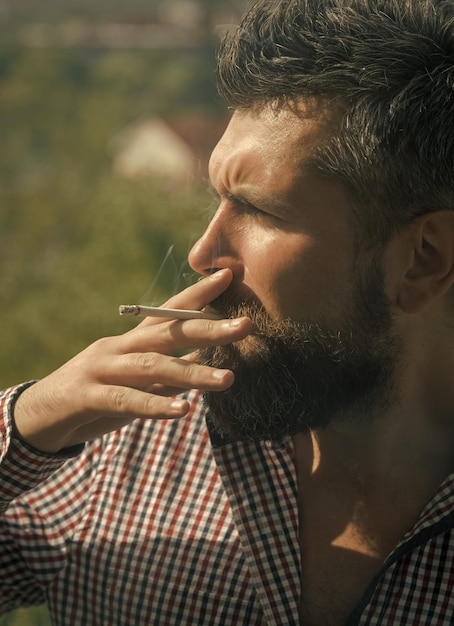 Hombre fumador fumando cigarrillo joven hipster barbudo con barba y bigote en cara seria fumando