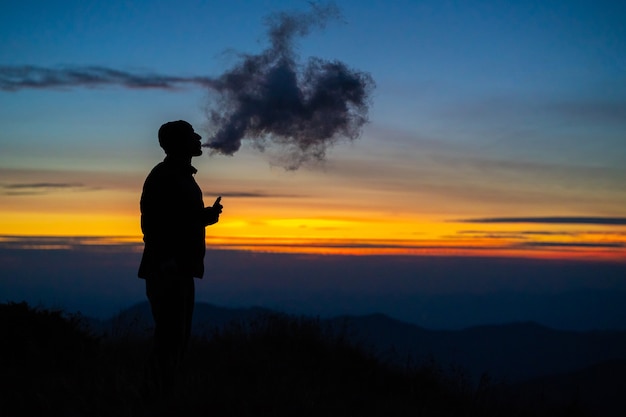 El hombre fumando un cigarrillo electrónico en el fondo del atardecer