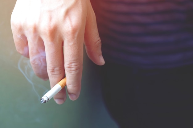 Foto el hombre fumando un cigarrillo en la mano. propagación del humo del cigarrillo.
