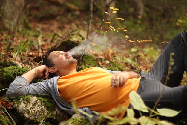 Foto hombre fumando mientras está acostado en el bosque