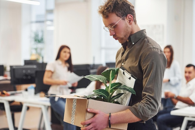 Hombre de gafas con caja está frente a gente de negocios que trabajan juntos en la oficina moderna.