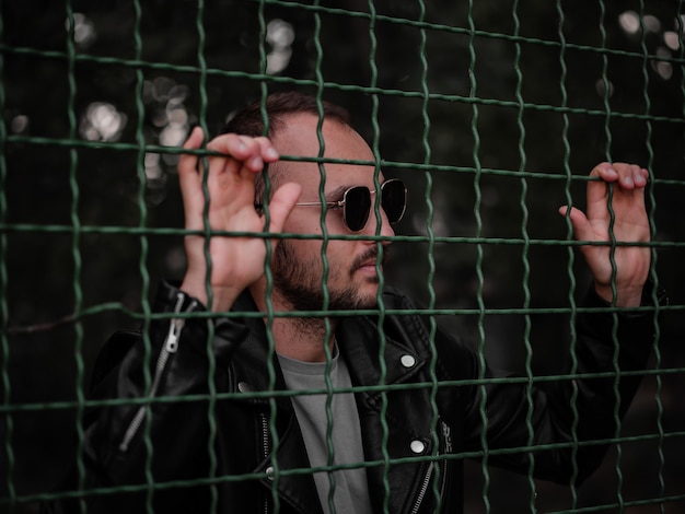 Foto un hombre con gafas y una chaqueta de cuero está detrás de una valla.