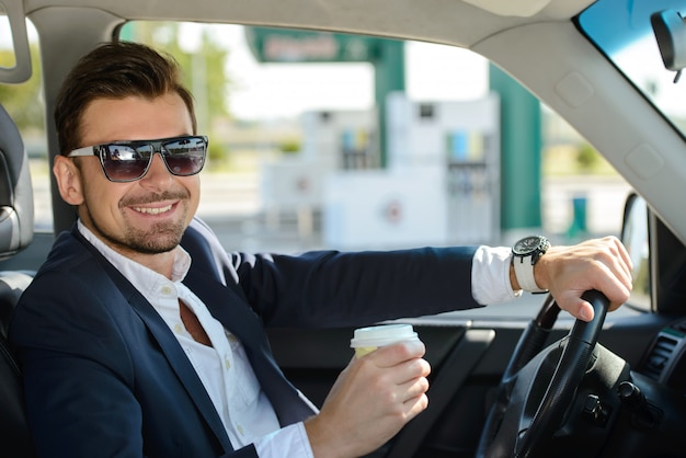 Un hombre con gafas está sentado en el coche y sonriendo.