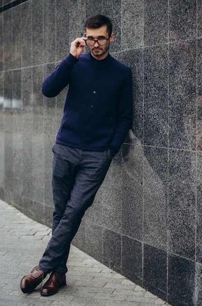 un hombre con gafas en la mano se para junto a la pared