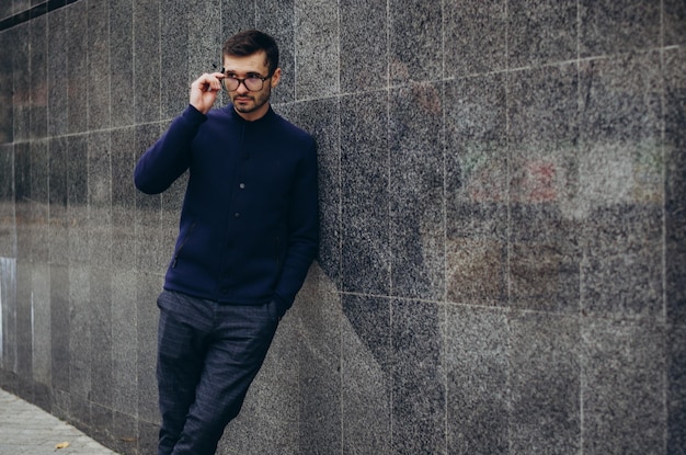 un hombre con gafas en la mano se para junto a la pared