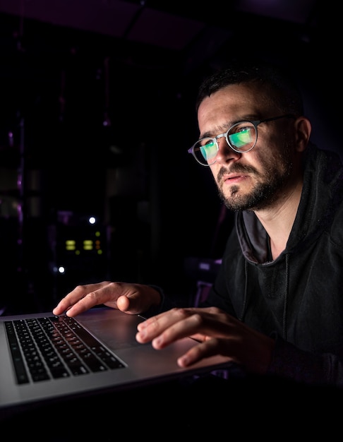 Un hombre con gafas en la oscuridad mira la pantalla de la computadora, copie el espacio.