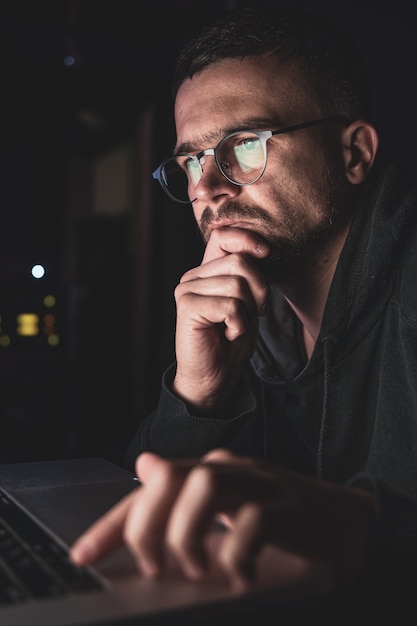 Un hombre con gafas en la oscuridad mira la pantalla de la computadora, copie el espacio.