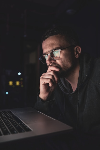 Un hombre con gafas en la oscuridad mira la pantalla de la computadora, copie el espacio.