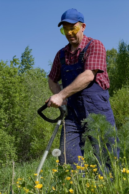 Un hombre con gafas protectoras corta la hierba con una cortadora de césped Cortando hierba Un agricultor que trabaja