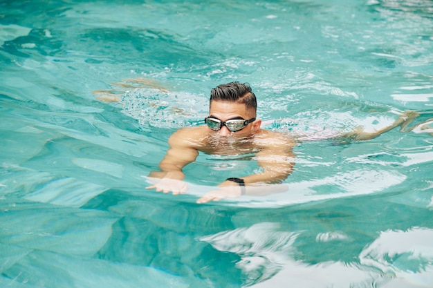 Hombre de gafas reflectantes nadando en la piscina del hotel o resort con agua turquesa