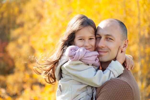 Hombre con gafas de sol abraza a hermosa hija en el fondo de coloridos árboles de otoño