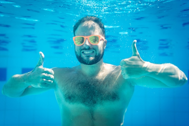 Hombre con gafas de sol amarillas bajo el agua dentro de una piscina