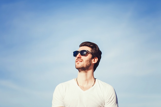 Hombre en gafas de sol y camiseta sobre cielo azul