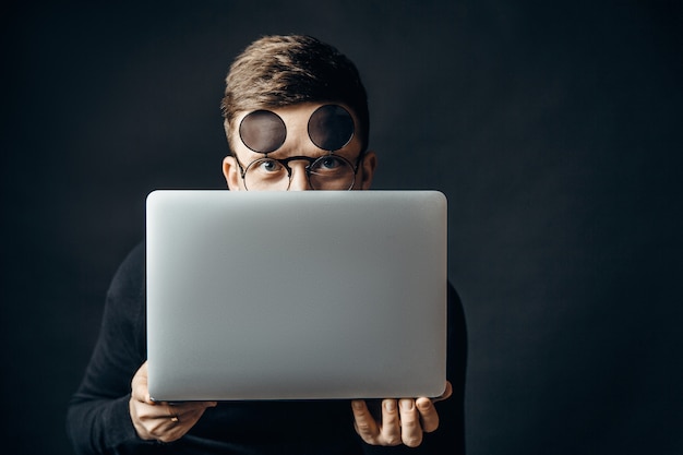 Hombre en gafas de sol escondiéndose detrás de la computadora portátil