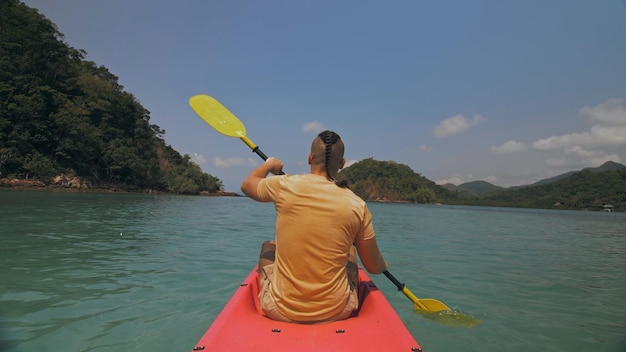 Foto hombre con gafas de sol filas de canoa de plástico rosa a lo largo del mar contra verdes islas montañosas con selvas salvajes