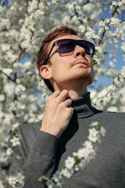 Un hombre con gafas de sol se para frente a un árbol en flor