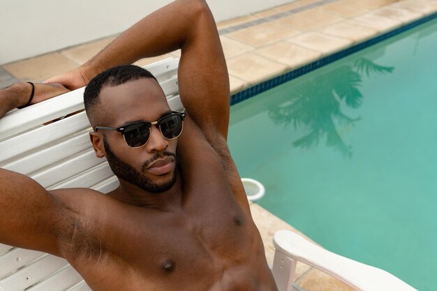 Hombre con gafas de sol relajándose en una silla de sol cerca de la piscina