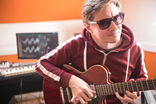 Un hombre con gafas tocando la guitarra y grabando una canción en el estudio.