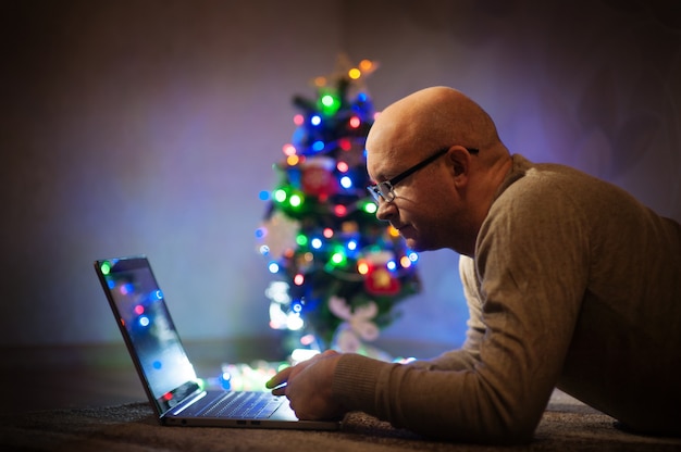 Hombre con gafas trabajando en una computadora portátil cerca del árbol de Navidad