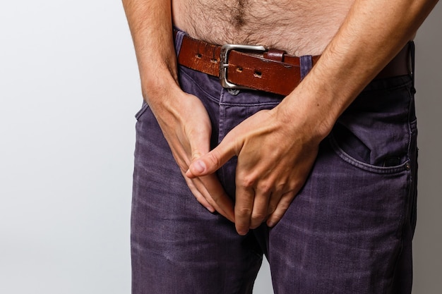 Foto hombre con ganas de ir al baño y sosteniendo su ingle sobre fondo blanco.