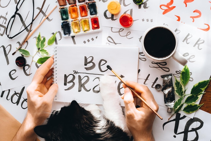 Foto hombre gato escribiendo en una hoja de papel palabra caligrafía ser valiente dibujando con tinta negra pincel artista creativo