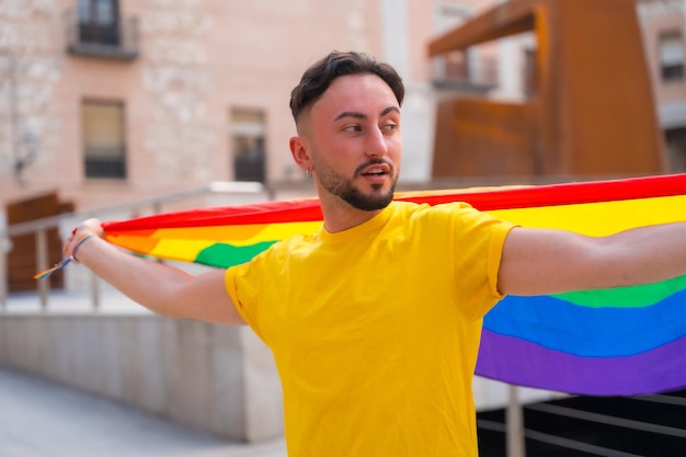 Hombre gay atractivo con la bandera lgbt del arco iris en la fiesta del orgullo de la ciudad y homosexual