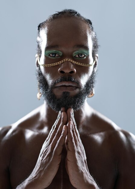 Hombre gay negro barbudo con maquillaje uniendo manos en el estudio azul