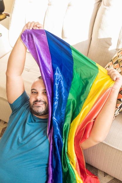 Hombre gay sentado en un sofá en casa con bandera lgbt