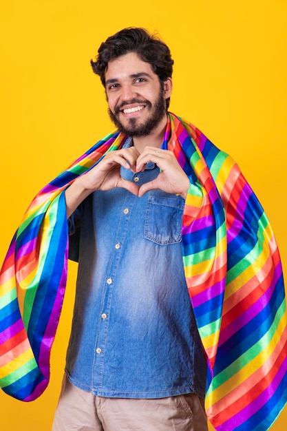 Foto hombre gay sonriendo mirando a la cámara haciendo un corazón con la mano