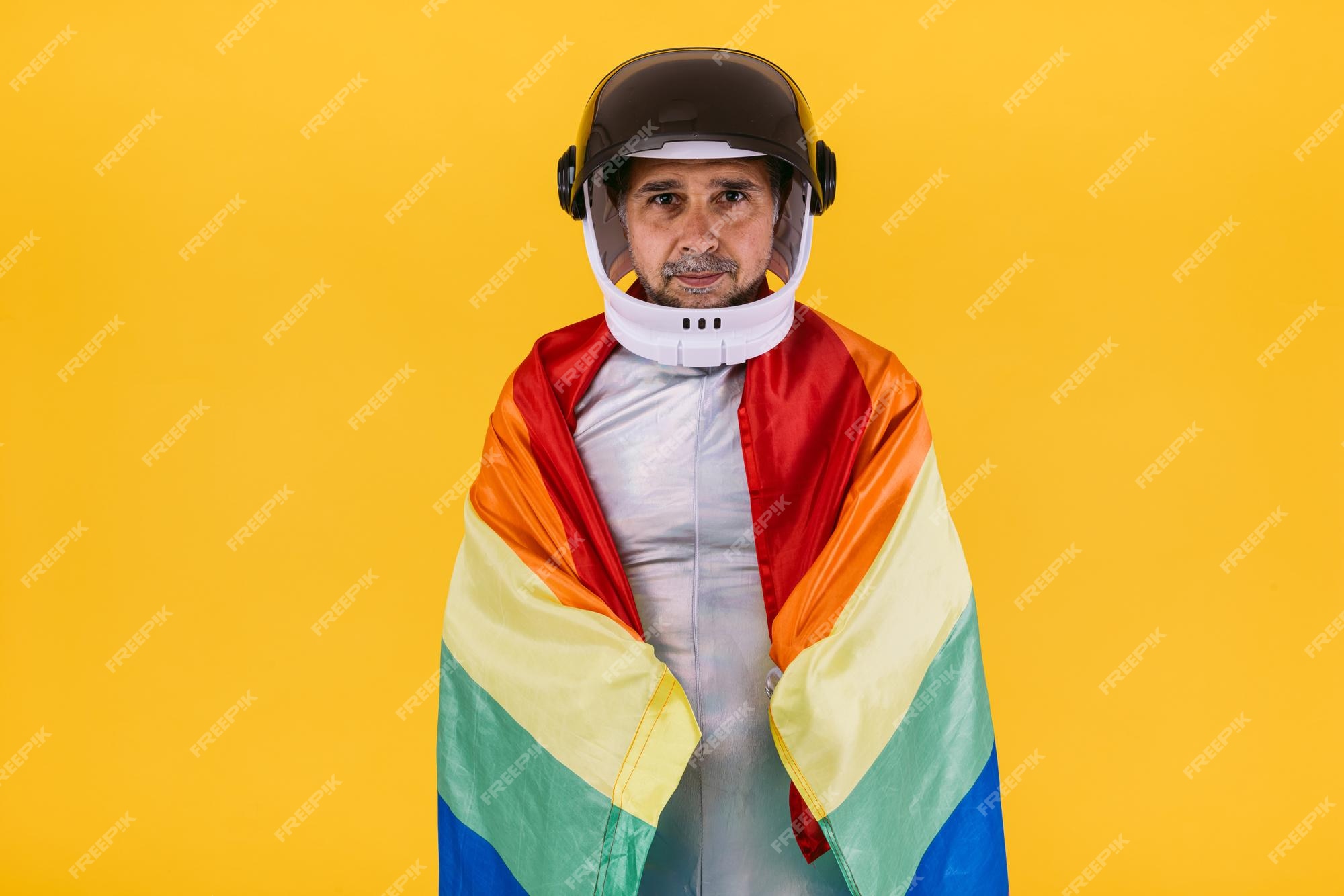 Hombre gay vestido como astronauta con casco y traje plateado con una  bandera colectiva arcoíris lgtbi sobre un fondo amarillo derechos  homosexuales trans homosexuales y concepto de orgullo de género | Foto