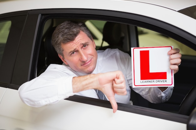 Foto hombre gesticulando pulgares hacia abajo con un cartel de conductor principiante