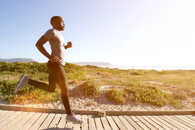 Hombre de gimnasio corriendo en el paseo marítimo en la playa