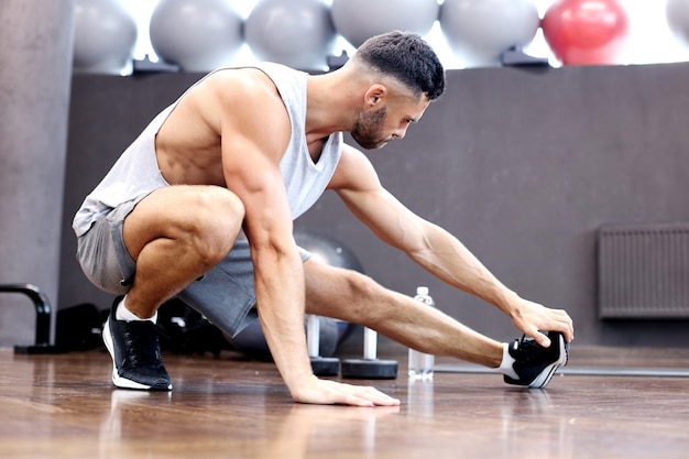 Hombre en el gimnasio haciendo ejercicios de estiramiento en el suelo.