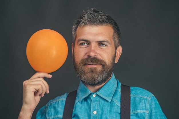 Hombre con globo naranja feliz barbudo en camisa de mezclilla azul y globo inflable en la mano