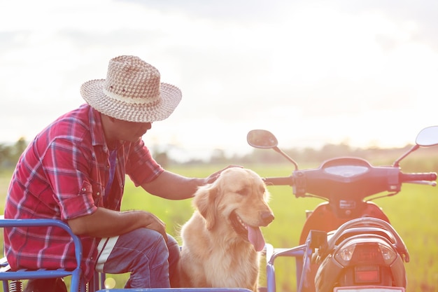 Hombre y golden retriever en motocicleta local en el campo de arroz por la noche