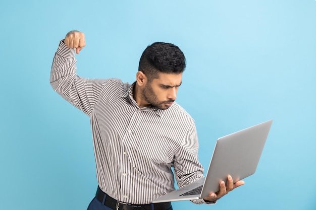 El hombre golpeando la pantalla de la computadora portátil se ve con una expresión enojada que amenaza con golpear mientras recibe una llamada