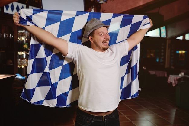 Hombre gordo alegre con una gran barriga con una bandera del Oktoberfest y un sombrero bávaro