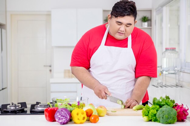 Hombre gordo asiático cortando un pepino en la cocina